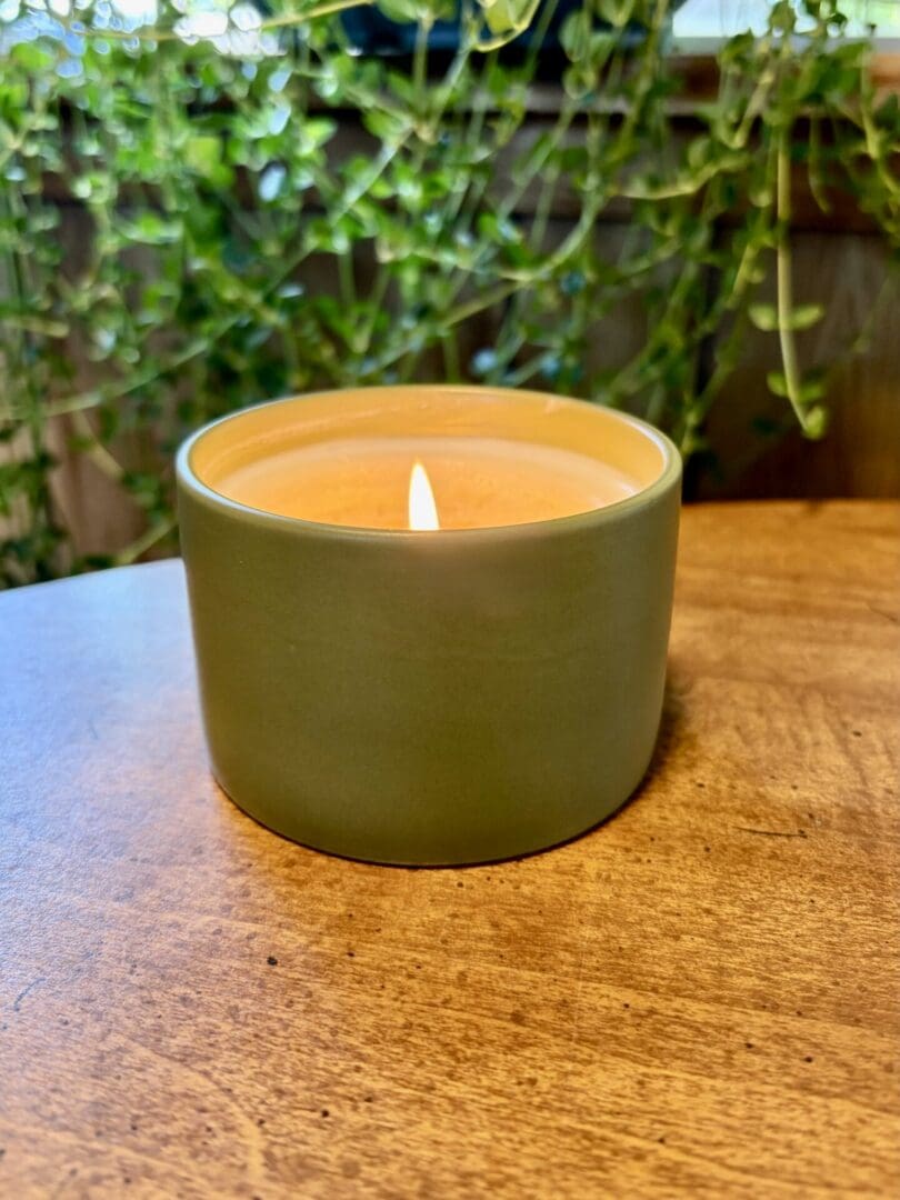 Handmade olive green candle with a warm glowing flame surrounded by hanging green plant